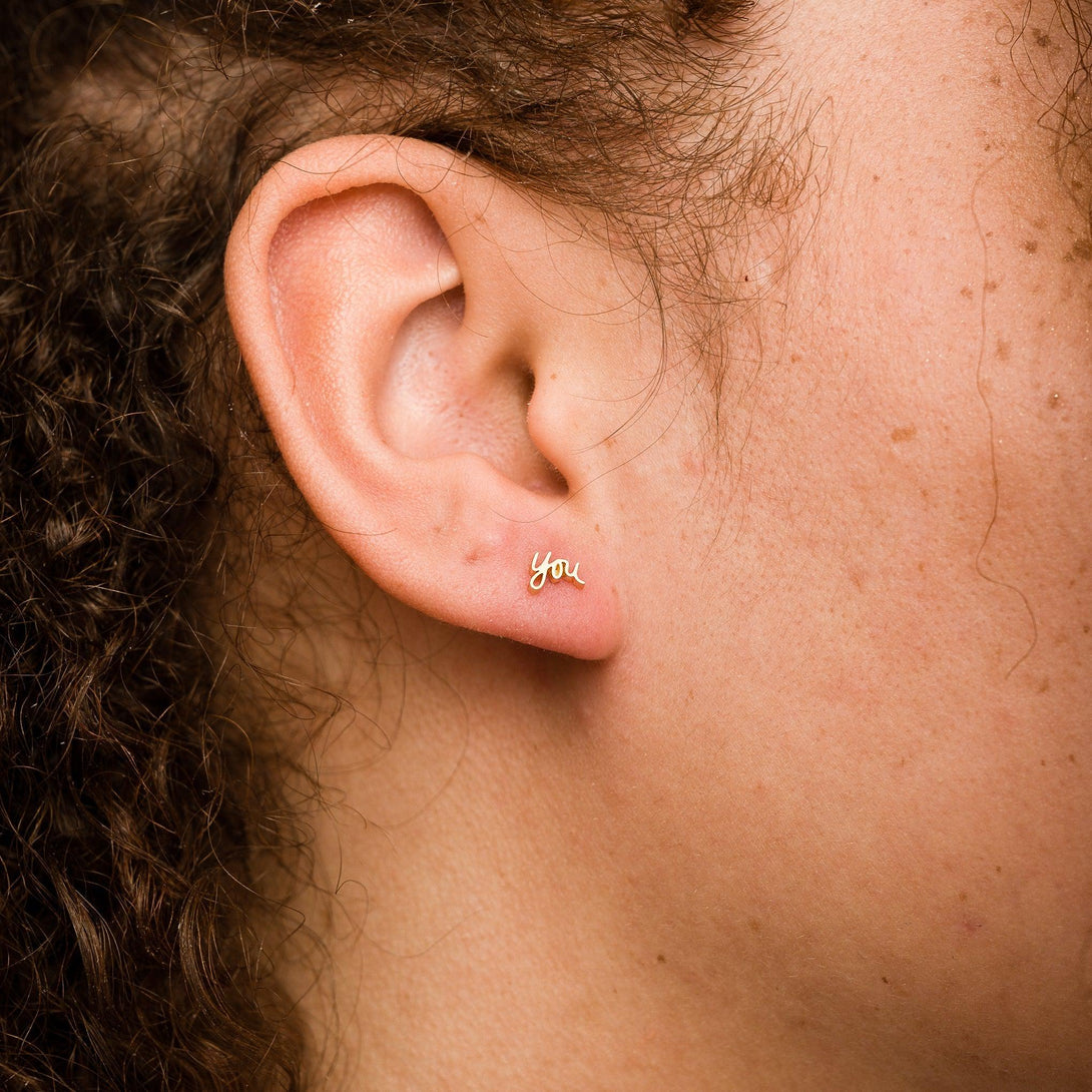 Close-up of a woman with dark hair wearing Gold You Script Stud Earring on her right ear.