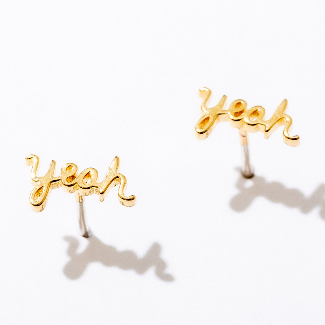 Gold Yeah Script Stud Earrings by Larissa Loden against a white background