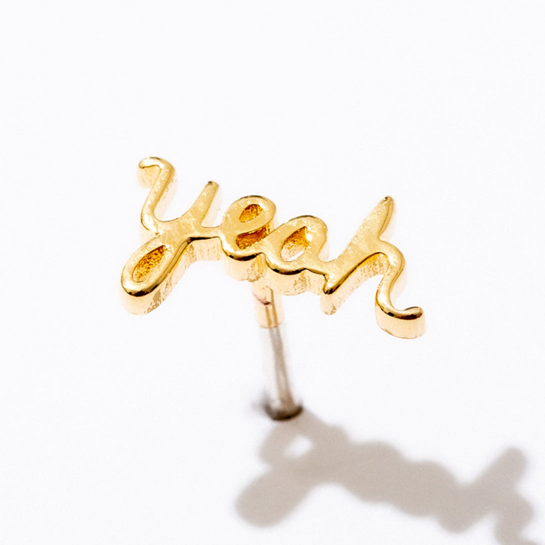 Single Gold Yeah Script Stud Earring against a white background, casting a shadow.